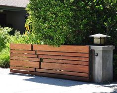 a wooden fence with a lantern on top in front of some bushes and trees,