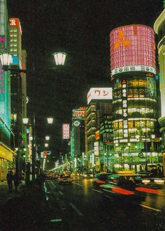 the city street is lit up at night with neon signs and buildings in the background