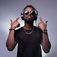 a man wearing headphones making the peace sign with his hands while standing against a gray background