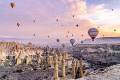 many hot air balloons are flying in the sky above some rocks and cliffs at sunset