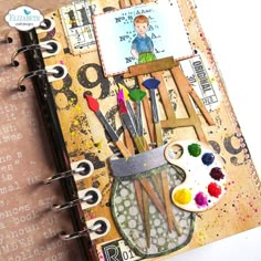 an art journal with paint and brushes on the cover, along with some other things