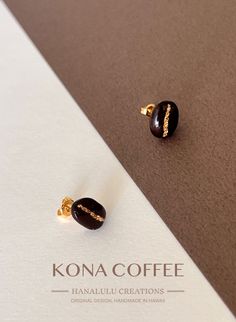 two small black and gold earrings sitting on top of a white paper with the words kona coffee written across it