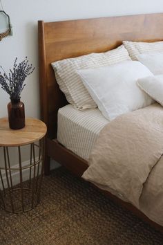 a bed with white sheets and pillows next to a small table on the carpeted floor