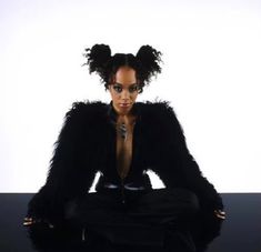 a woman sitting on top of a table in front of a white wall wearing black clothing