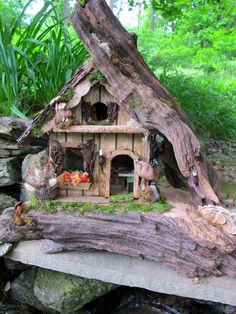 a small house made out of logs in the middle of some trees and rocks with water running through it