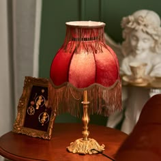 a red lamp sitting on top of a wooden table next to a framed photo and a golden frame