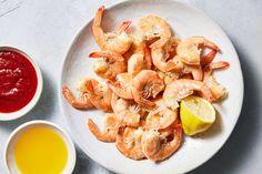 a white plate topped with cooked shrimp next to a bowl of ketchup and a lemon wedge