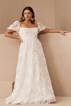 a woman in a white wedding dress leaning against a wall with her arms out and looking at the camera