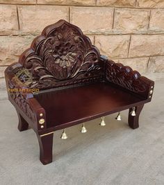 an ornately carved wooden bench with bells on the legs and foot rests in front of a stone wall