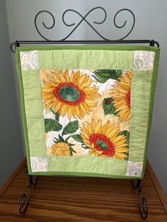 a green and yellow sunflower quilt hanging from a metal rack on top of a wooden table