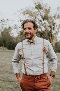 a man wearing suspenders and a bow tie standing in the grass with his hands on his hips