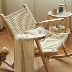 a rocking chair with a blanket on it next to a table and vase filled with flowers