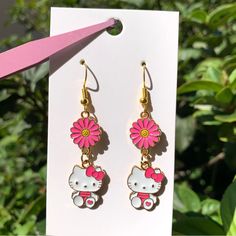 a pair of hello kitty dangle earrings with pink flowers in the shape of a car