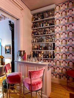 two pink chairs sitting in front of a bar with bottles on the wall behind it