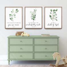 three framed art prints on the wall above a dresser with a rocking horse and baby's crib