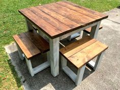 a wooden table and two benches sitting on the sidewalk in front of a grassy area