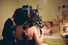 a woman sitting on a bed with a camera attached to her head and two other people in the background