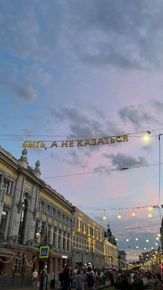 people are walking down the street in front of buildings with lights strung from them and there is a sign that says, let's a he easter