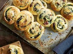 several muffins with spinach and cheese are on a baking sheet next to a cutting board