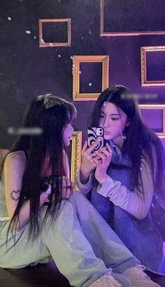 two young women sitting on the floor looking at their cell phones in front of a mirror