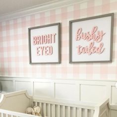 a baby's room with pink and white wallpaper, two framed pictures above the crib