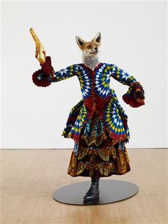 a sculpture of a fox holding a piece of wood in its hands and wearing a colorful dress