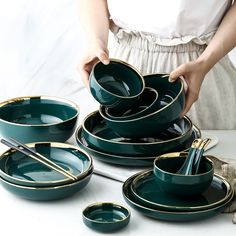 a woman is setting green dishes with gold trimmings on the edges and sides