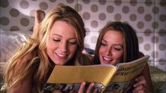 two beautiful young women laying in bed reading a book