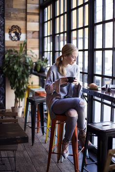 a woman is sitting on a stool using her cell phone in a restaurant with lots of windows