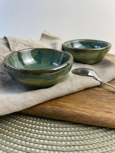 two green bowls with spoons sitting on top of a wooden table