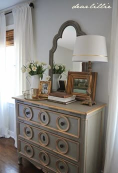 an old dresser with some pictures on it and a lamp in front of the mirror