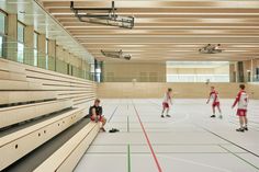 several young boys are playing basketball in an indoor gym with wooden benches and large windows