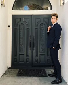 a man standing in front of a door wearing a suit and looking at the camera