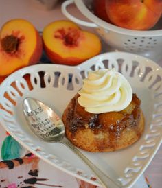 a plate topped with a pastry next to two peaches and a measuring cup filled with whipped cream