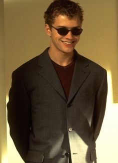 a man wearing sunglasses standing in front of a white wall