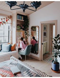 two people sitting at a desk in a room with plants on the window sill