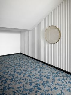 an empty room with striped walls and blue carpeted flooring in front of a round mirror