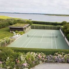 an aerial view of a tennis court surrounded by greenery and flowers with the ocean in the background