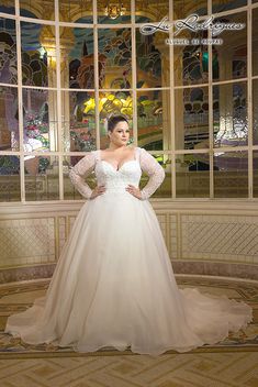 a woman standing in front of a window wearing a wedding dress with long sleeves and beading