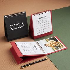 two calendars and a pen sitting on top of a table next to each other