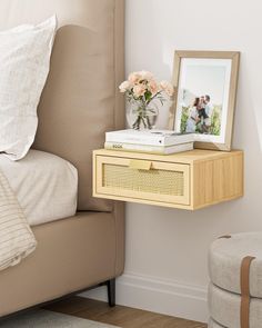 a nightstand with flowers on it next to a bed and a framed photo in the corner