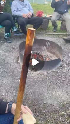 people sitting around an open fire pit with a stick sticking out of the ground next to it