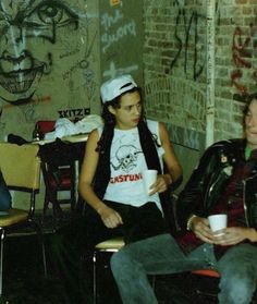 two people sitting in chairs with graffiti on the wall and one person holding a coffee cup