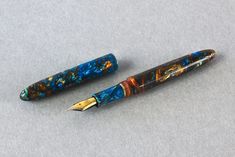 two fountain pens sitting next to each other on top of a gray surface with gold trimming