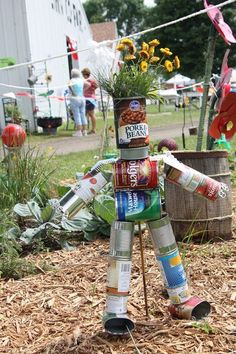 a tin can robot made out of cans in the middle of a yard with people standing around