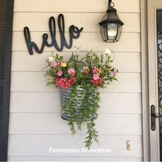 flowers in a basket hanging on the side of a house next to a lamp and door