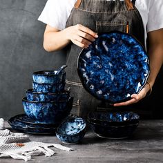 a person holding a blue plate with six bowls on it and five plates stacked in front of them