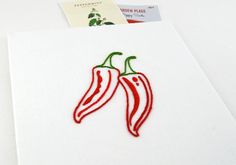 two red peppers embroidered on white paper next to a postcard with the word pepper written on it