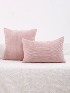 two pink pillows sitting on top of a white bed next to each other in front of a white wall