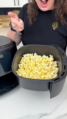 a woman with curly hair holding a bowl of popcorn in front of an air fryer